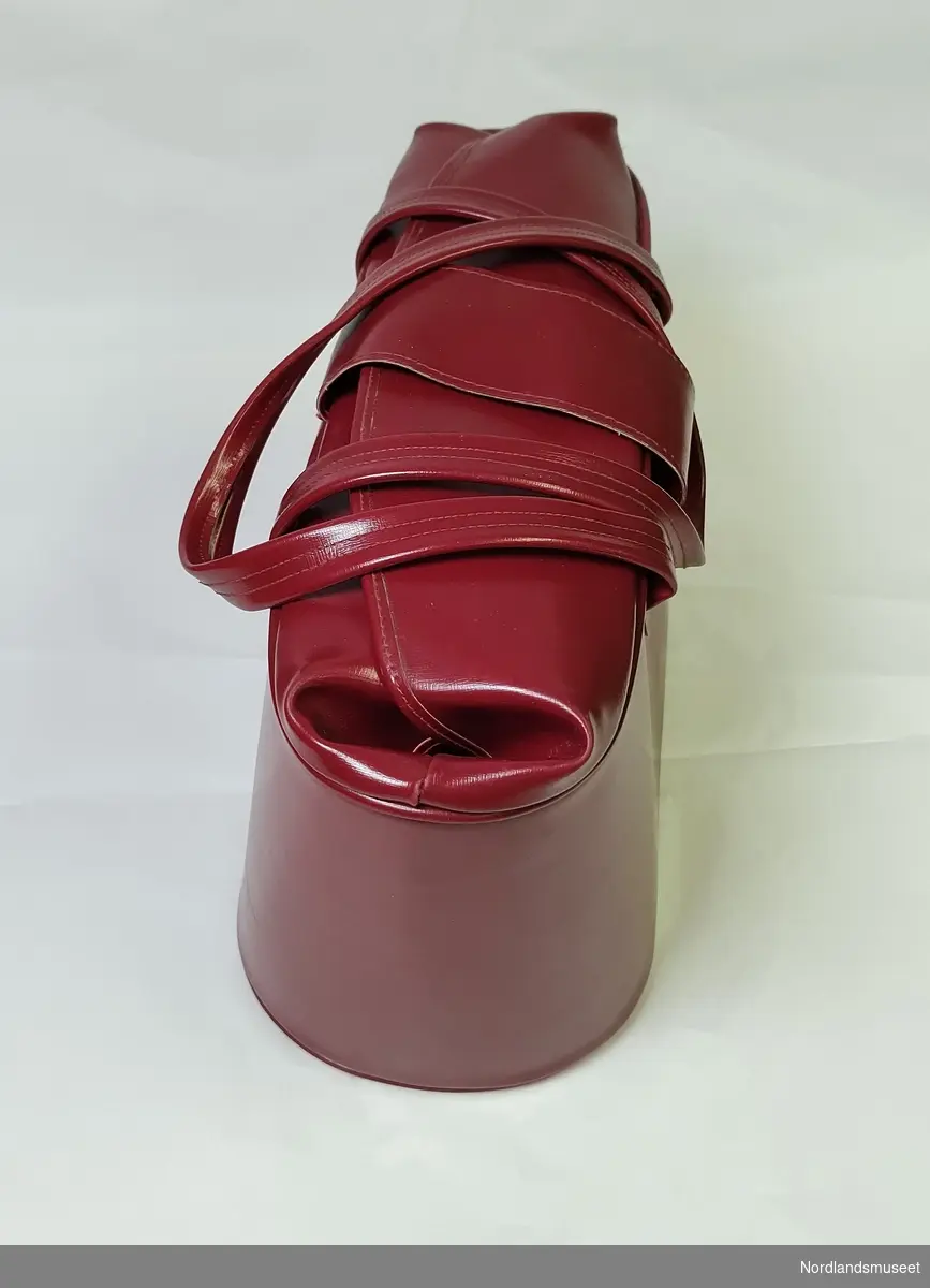 Rød veske med to korte reimer og lås på fremsiden. 
Vesken er i stivt matriale og har fem knotter under.