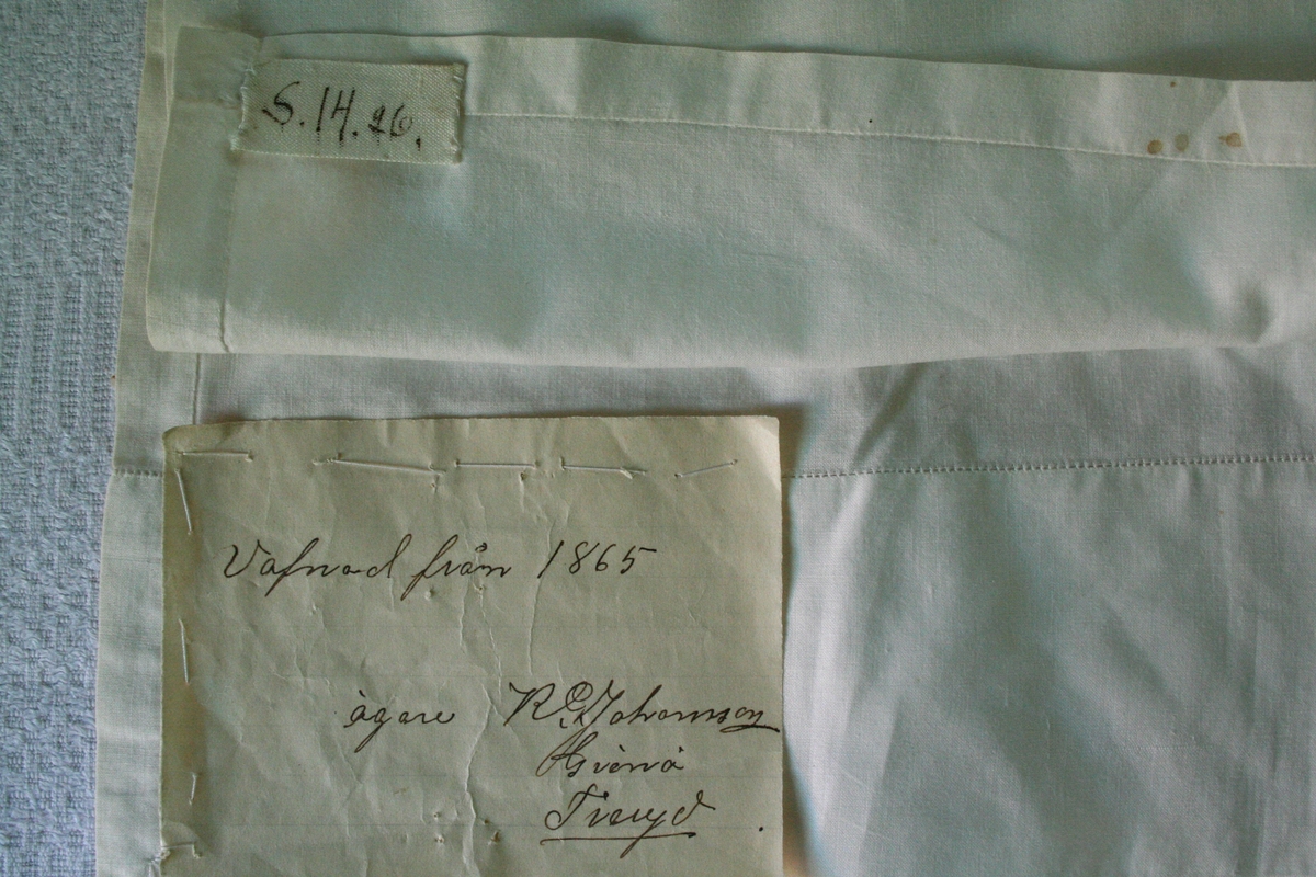 Kvadratiskt hals-eller huvudkläde av fin linne- eller bomullslärft. På två motstående sidor 7,2 cm bred fåll sydd med enkel hålsöm, på två sidor smal fåll.
Anteckning på påsydd lapp: Gammalt kläde från 1841.

Påsydd märkning S.14.26 troligen förväxlad märklapp.

Ingår i Textilinventeringen i Kronobergs län 1928-1930,
S.14.12, ägare Karl Johansson, Grönö.

/Birgitta Blixt 2022