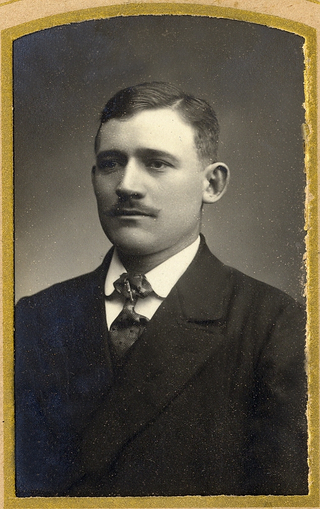 En man i mörk kostym med stärkkrage och slips. Under fotot text med