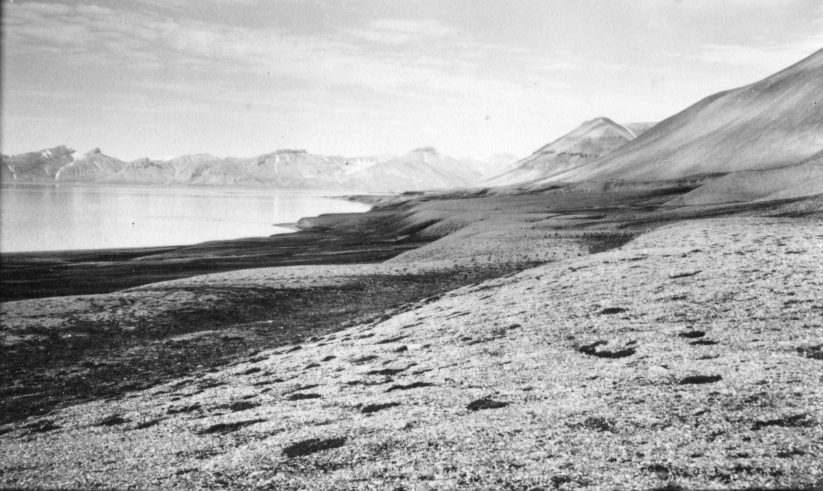 Utsikt mot Kapp Ekholm fra Phantomodden. Bildet kommer fra The Cambridge Spitsbergen Expedition. Ekspedisjonen besto av seks menn, de fleste var geomorfologer, som dro fra England til Svalbard via Nordkapp og Bjørnøya om bord på Lyngen sommeren 1938. Målet deres var å kartlegge området rundt Nordenskioldbreen, Gipsvika og Brucebyen.