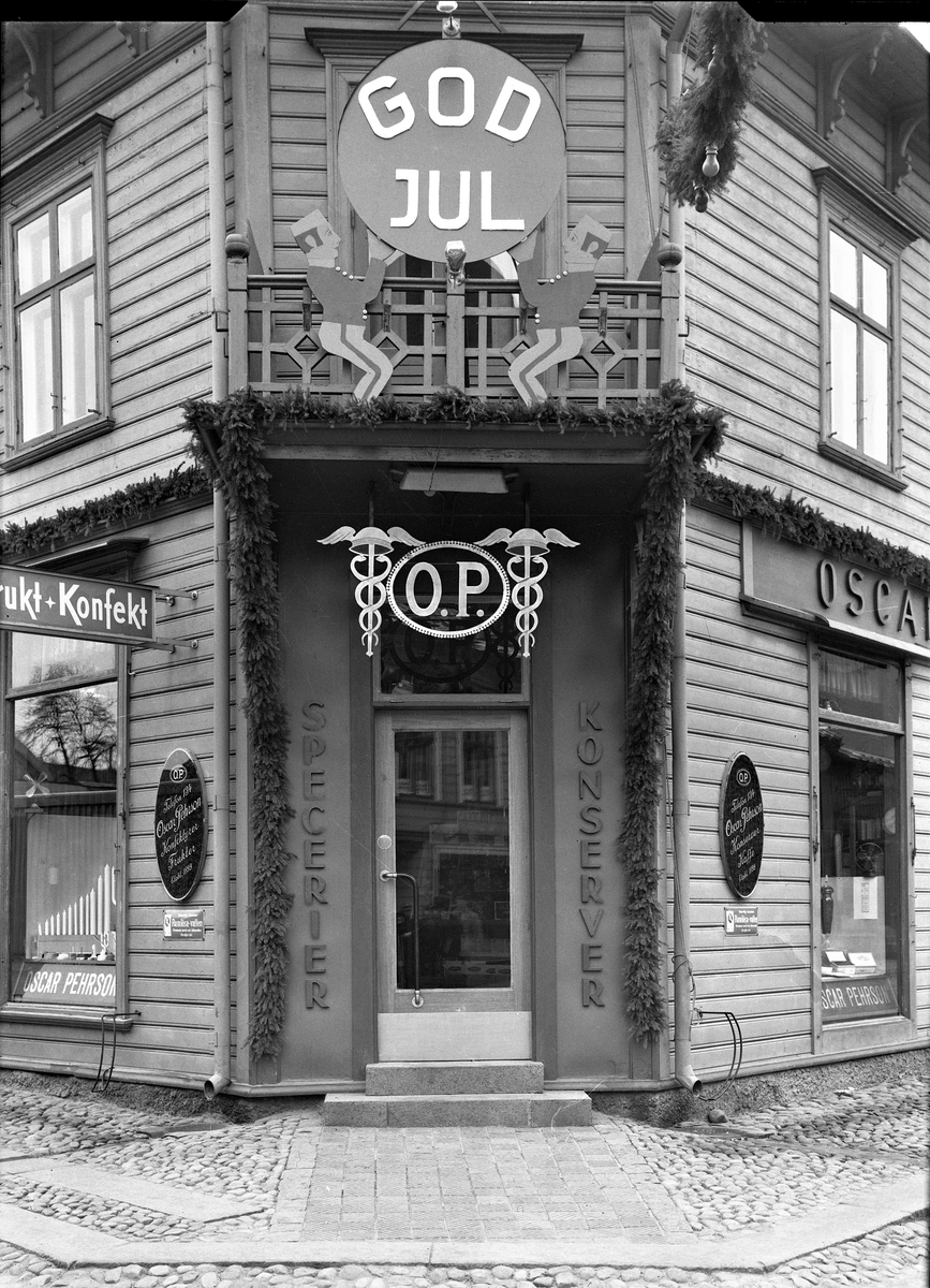 Julskyltad entré till OP:s speceriaffär som låg i hörnet Norrgatan-Kungsgatan, kv Lagmannen. Oscar Pehrson startade sin butik 1899 och i sin exteriöra reklam lyfter han fram frukt, konfekt, specerier och konserver.