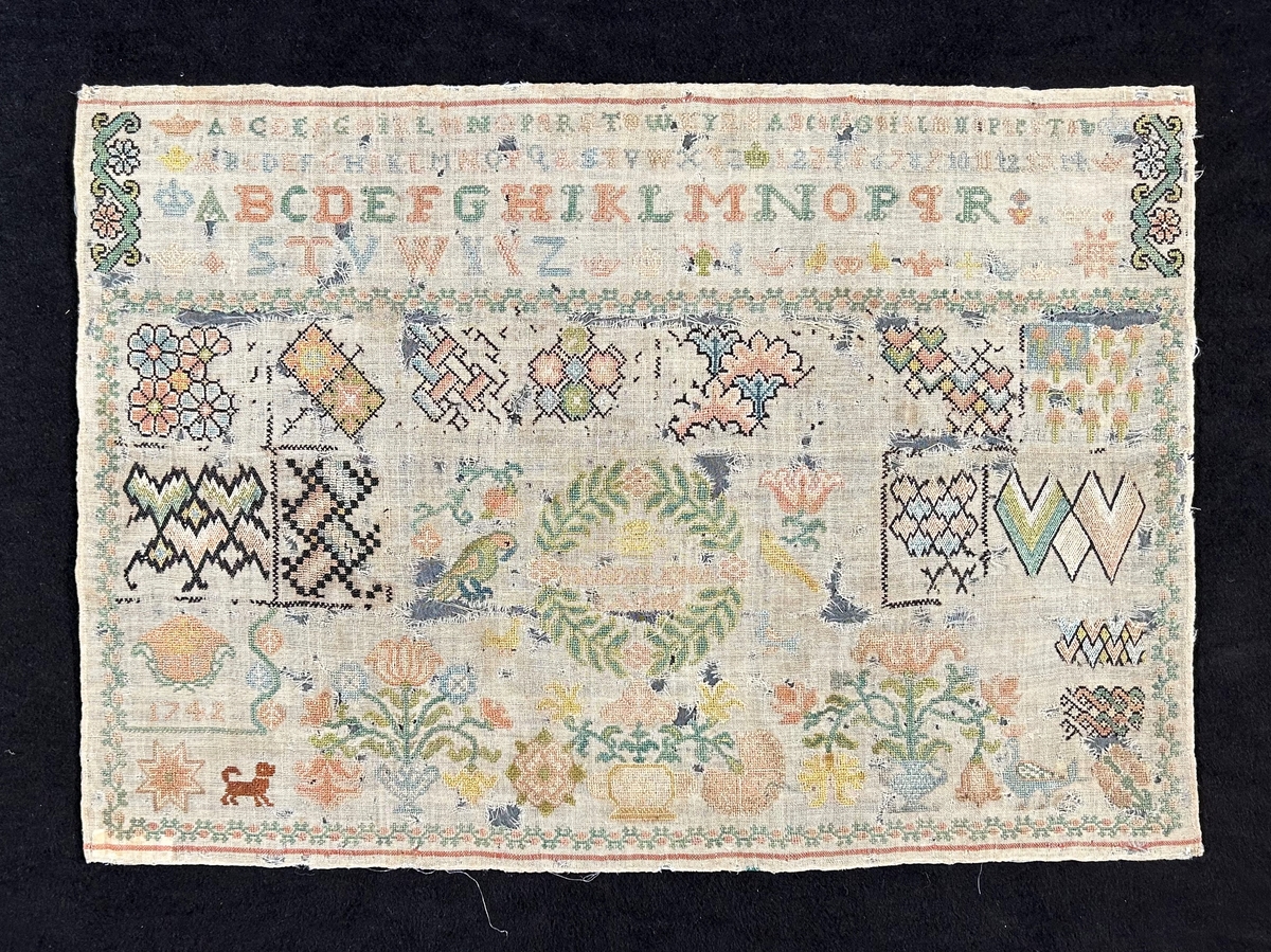 Märkduk i rektangulär form av naturfärgat ylle och broderad med silke i färgerna grönt, rosa, blått, brunt, gult, beige och svart. Kors- och gobelängsöm. Överst alfabetet i två olika storlekar, hörn och kantdekor, den övriga delen av duken upptar blom- och djurmotiv samt geometriska figurer, inom en bladkrans står "Margareta Bagge". I nedre vänstra hörnet står årtalet 1742.
