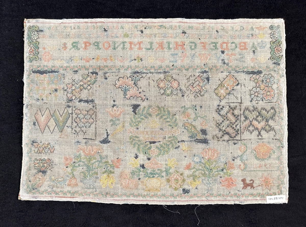 Märkduk i rektangulär form av naturfärgat ylle och broderad med silke i färgerna grönt, rosa, blått, brunt, gult, beige och svart. Kors- och gobelängsöm. Överst alfabetet i två olika storlekar, hörn och kantdekor, den övriga delen av duken upptar blom- och djurmotiv samt geometriska figurer, inom en bladkrans står "Margareta Bagge". I nedre vänstra hörnet står årtalet 1742.