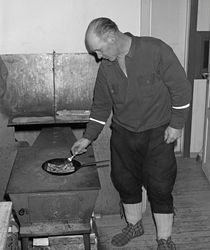 Skogsarbeider lager middag i koia. Johan Rasch steker flesk 