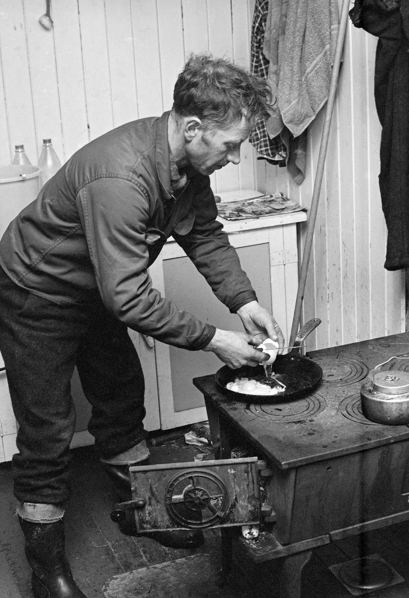 Matlaging i Østlikoia i Løiten almenning (Løten allmenning) i februar 1977. Fotografiet er tatt inne i koierommet. Asmund Pedersen steiker speilegg.