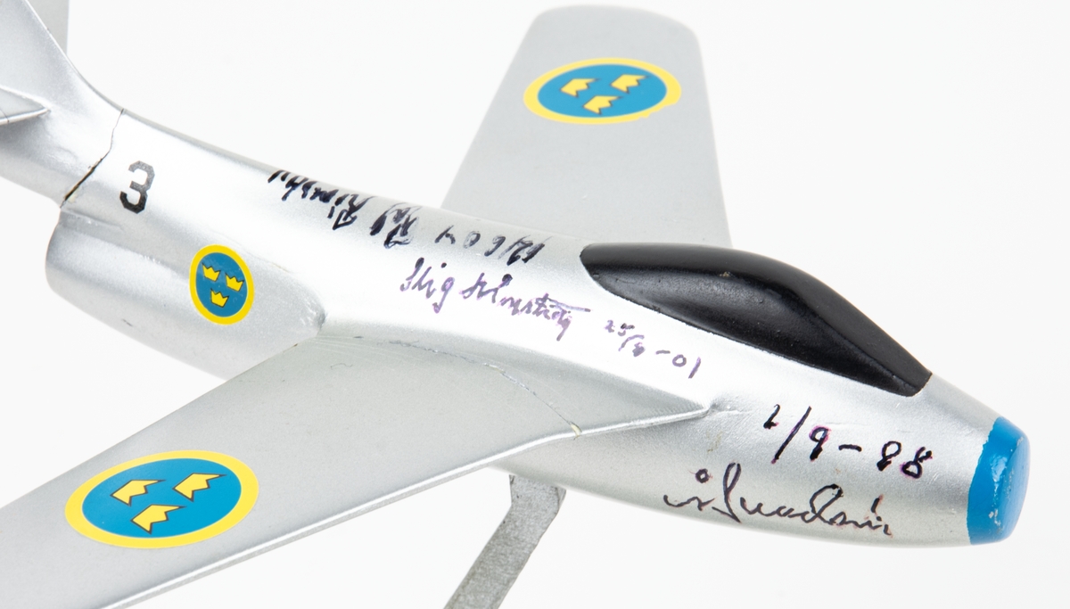 Flygplansmodell Tunnan med fot. På flygplanskroppen finns namnteckningar och årtal.