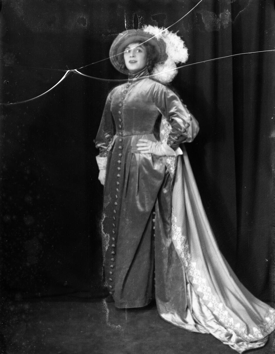 Portrett av skuespilleren og sceneinstruktøren Gerda Ring. Hun poserer i kjole med slep og hatt med fjær.
