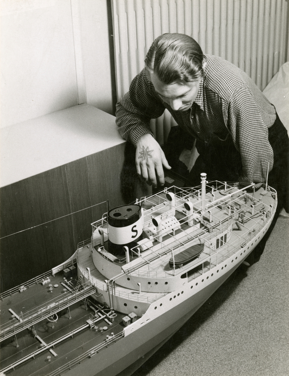 Utställning i Sjöfartsavdelningen, avdelning för Nyare varv. En ung man med en tatuerad kompassros på handen tittar på fartygsmodellen av SVEADROTT.