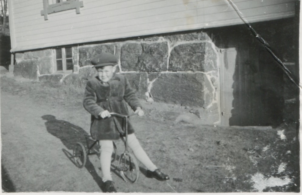 En liten gosse sitter på en trehjuling, Kållered Stom "Nygård" okänt årtal.