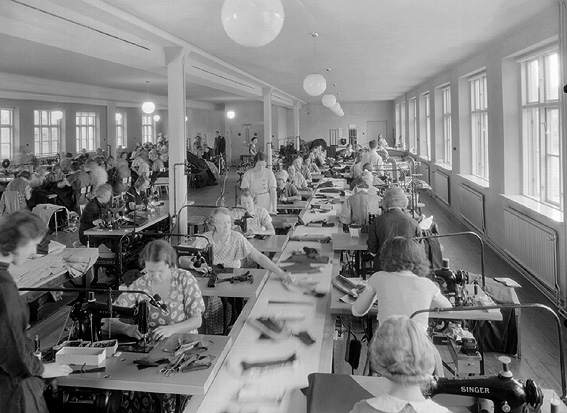A-B. Bergsson och söner; interiör av fabriken. Sömmerskor vid symaskiner.
Företaget som var känt över hela vårt land som ett av de större i konfektionsbranschen och grundades 1900 av framlidne grosshandlaren B.Bergsson och hans två äldsta söner som grosshandelsfirma i manufakturbranschen. 1914 upptogs egen tillverkning av herrkläder. 1929 skedde en första tillbyggand av fabrikslokalerna. Åren 1935-36 utökades fabrikslokalerna till det dubbla och företaget har kunnat glädja sig åt ett fullt utnyttjande av sin kapacitet c:a 40.000 plagg per år. Firman hade även upptagit tillverkning av damkappor och damdräkter.
Källa: Nyblom-Svanqvist, Näringsliv i Värmland.1945.