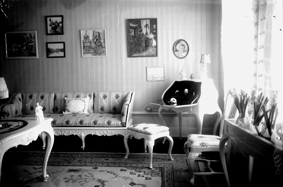 Salong möblerad med soffa, bord, en slags sekretär med taburett. Konstverk på väggarna.
Fotografens ant: Olssons, Höje.