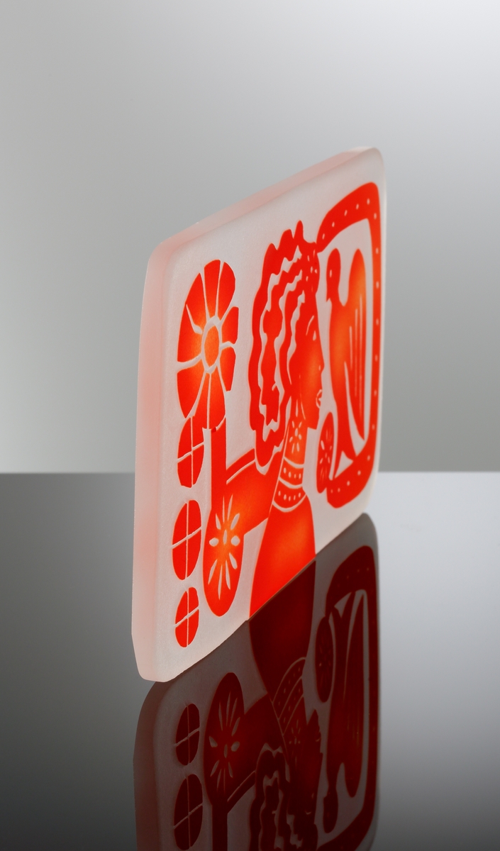 Formgiven av Edvin Öhrström. Platta med blästrad dekor av ”Flickan och Duvan” i röd färg. Troligen tänkt att ingjutas i ett glasblock.
