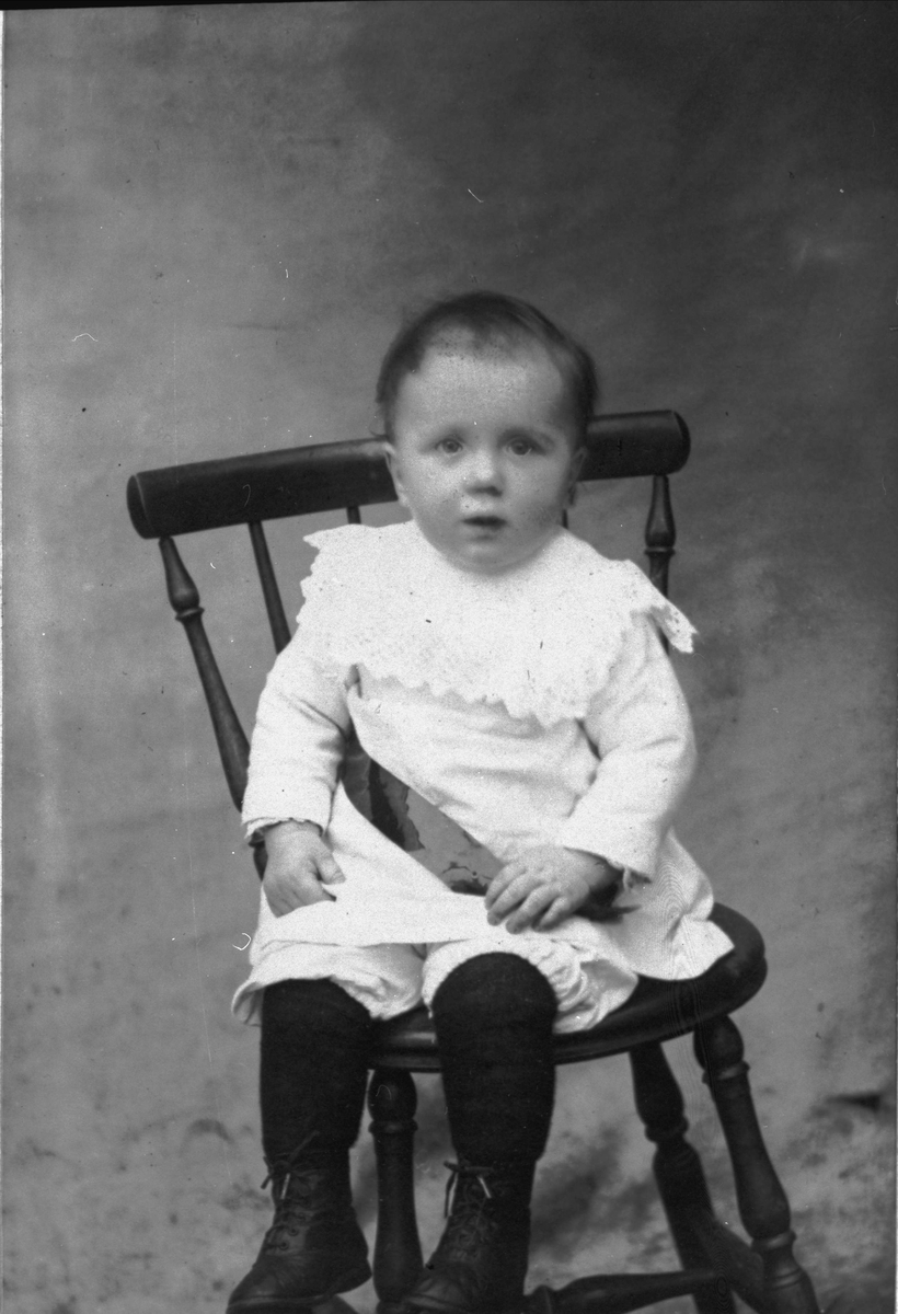 Studioportrett av liten gutt som sitter på en stol.