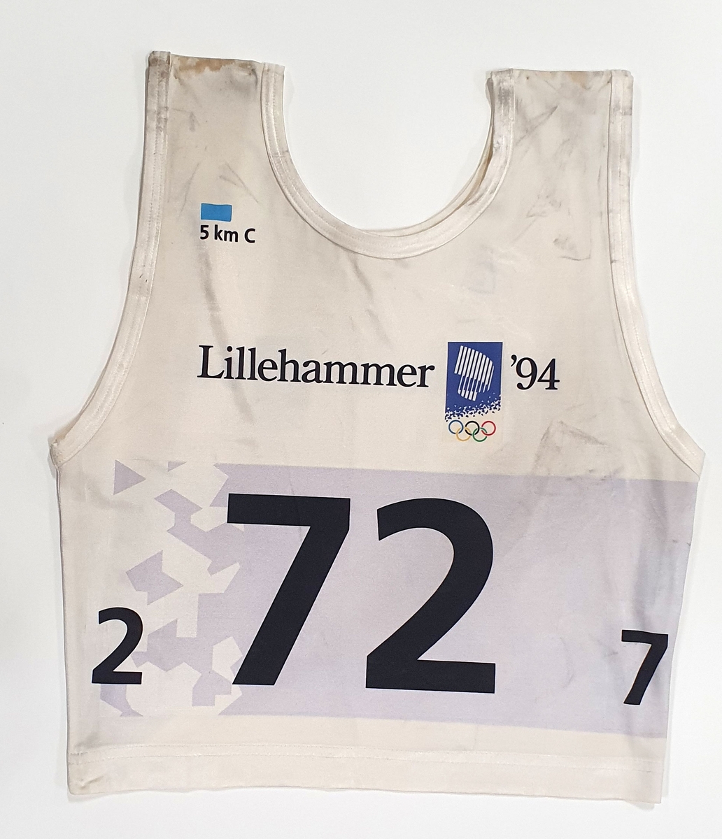 Hvitt startnummer utøver med nummer 72. Tallet er plassert i et grått felt med krystallmønster.  Emblem fra vinter-OL på Lillehammer 1994.