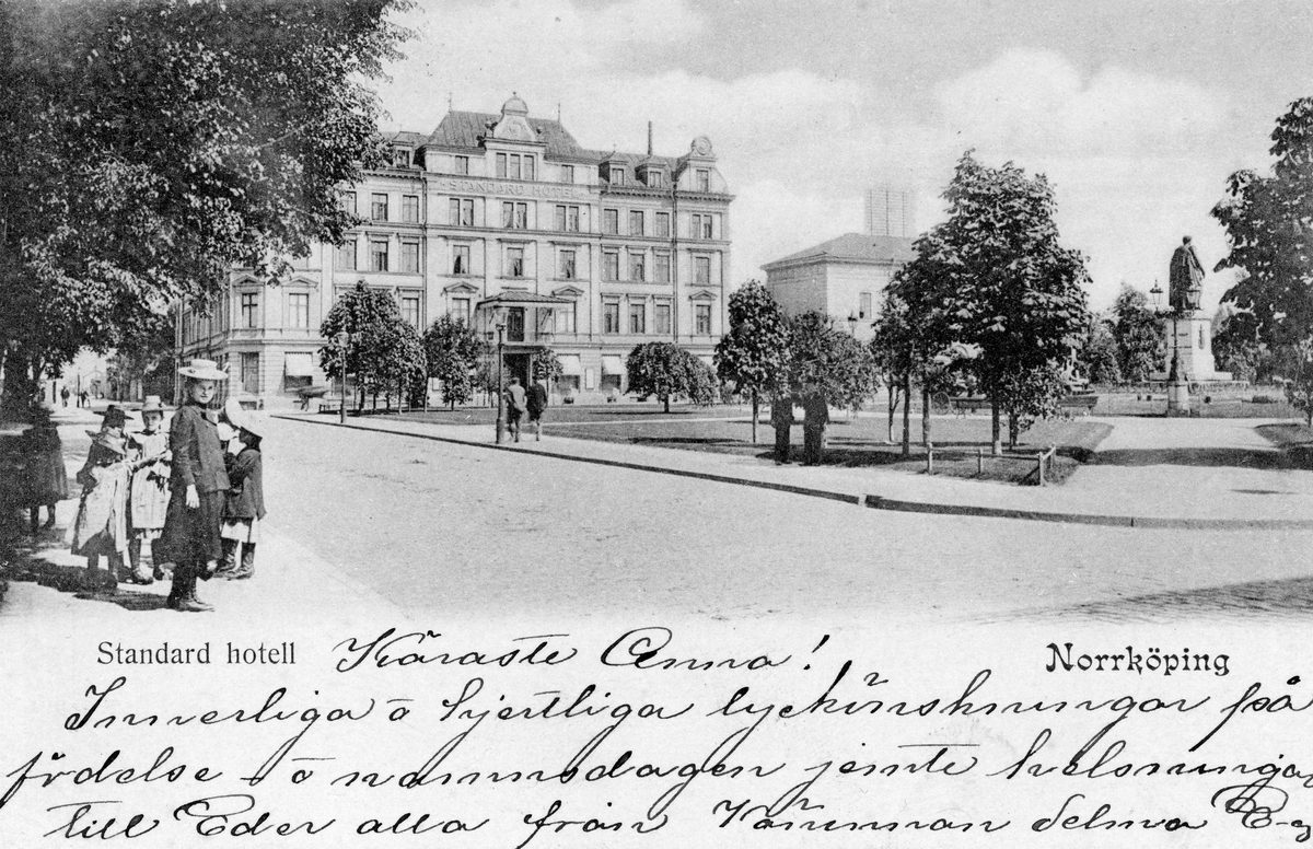 Brevkort med vy över Carl Johans park mot Standard hotell i Norrköping. En lyckönskning till slöjdlärarinnan Anna Jonsson i Skedevi från vännen Selma. Poststämplat 1903.