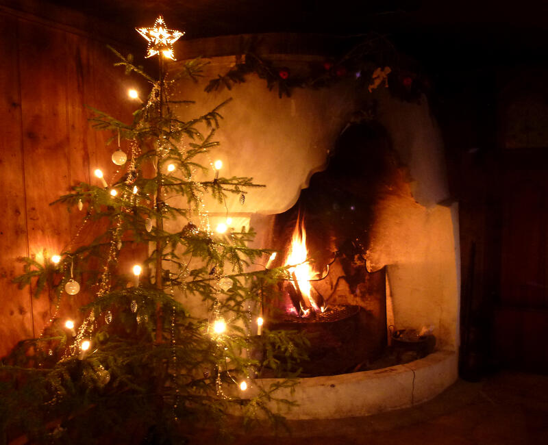 A fire is burning in an open fireplace, and a decorated Christmas tree is standing next to it.
