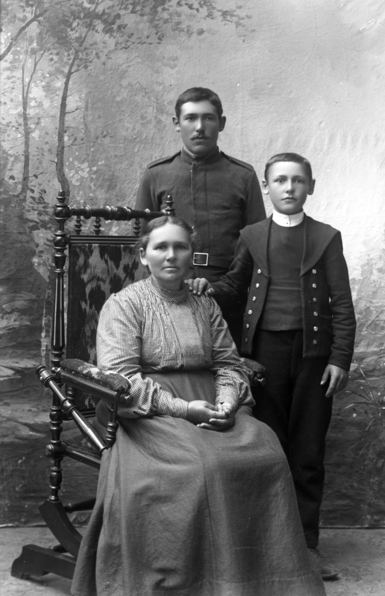 Atelierfoto.Helfigurer.En eldre kvinne sitter og en soldat og en gutt står ved. Familiebilde?