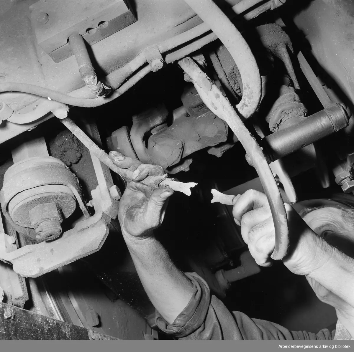 Oslo Sporveiers vognmateriell kontrolleres etter strenge rutiner i trikkehallen på Grefsen. "Ved kontrollen ble det oppdaget at kabelskoene på en jordledning hadde røket". August 1958