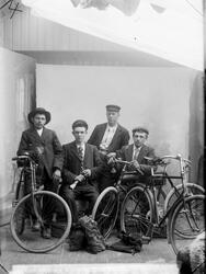 Gruppeportrett i studio av fire menn med sykler. M. Lehne.
