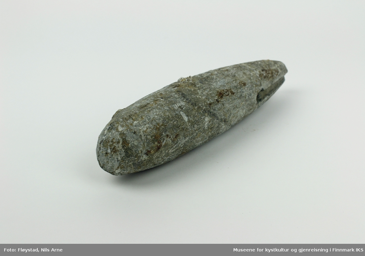 En avlang søkke, eller jarstein laget av stein med et gjennomgående hull og spor til snøre i den smale enden av steinen. Jarsteinen har en glatt overflate.