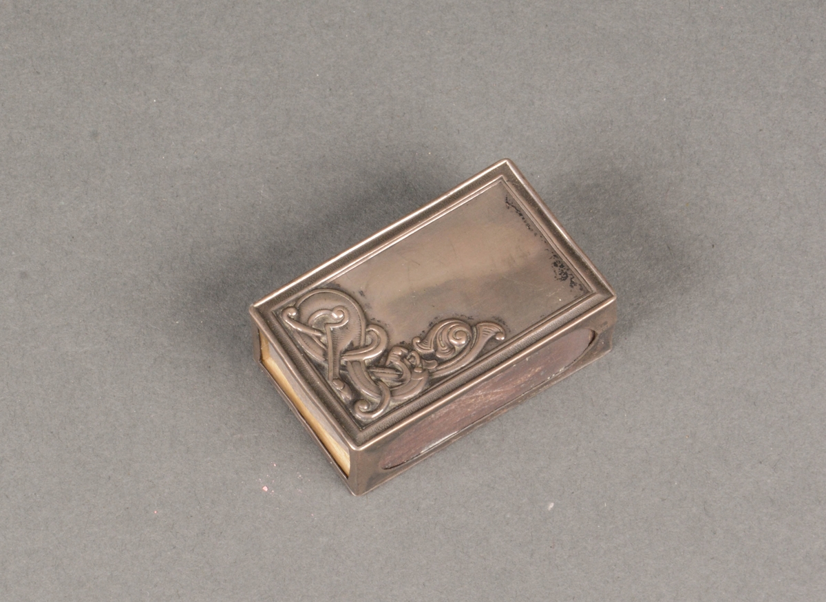 Kuvert fyrstikkeske med dragemønster i relieff på metallhylsen som dekker lokket.