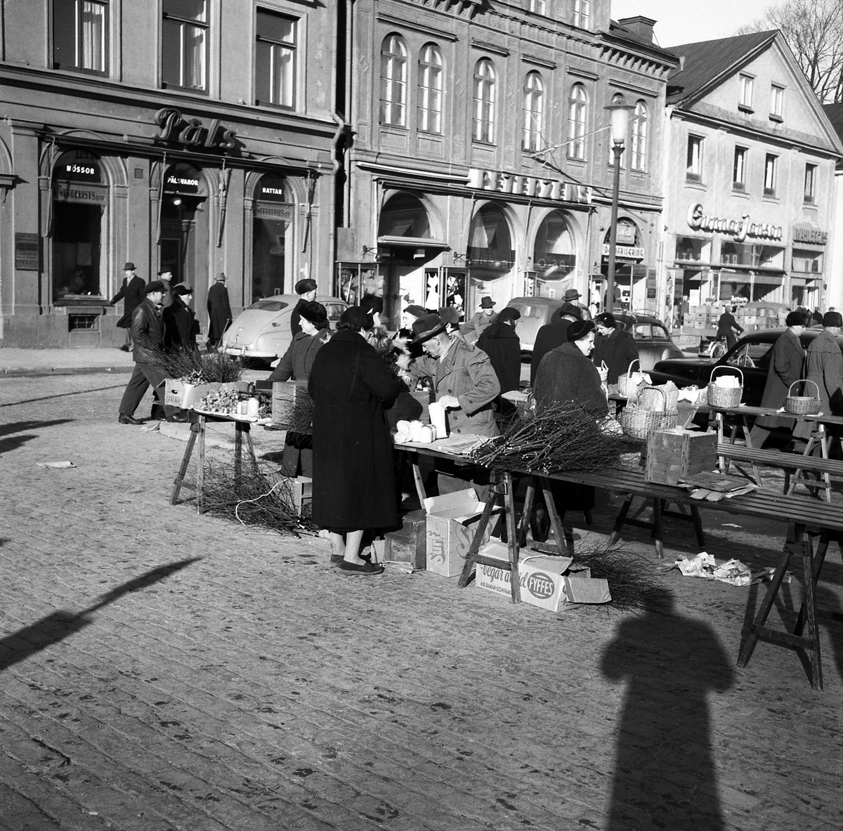 Livlig torghandel på Stora torget i Linköping vårvintern 1956. Hög tid att införskaffa ris till påsken. I fonden husraden utmed torgets västra sida.