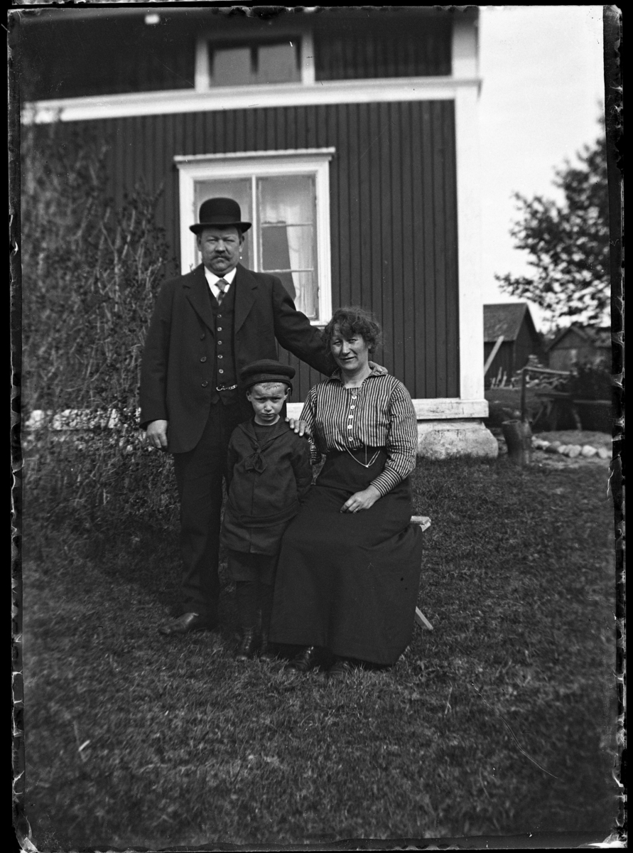 Familjeporträtt; en man, en kvinna och en pojke utanför ett bostadshus.