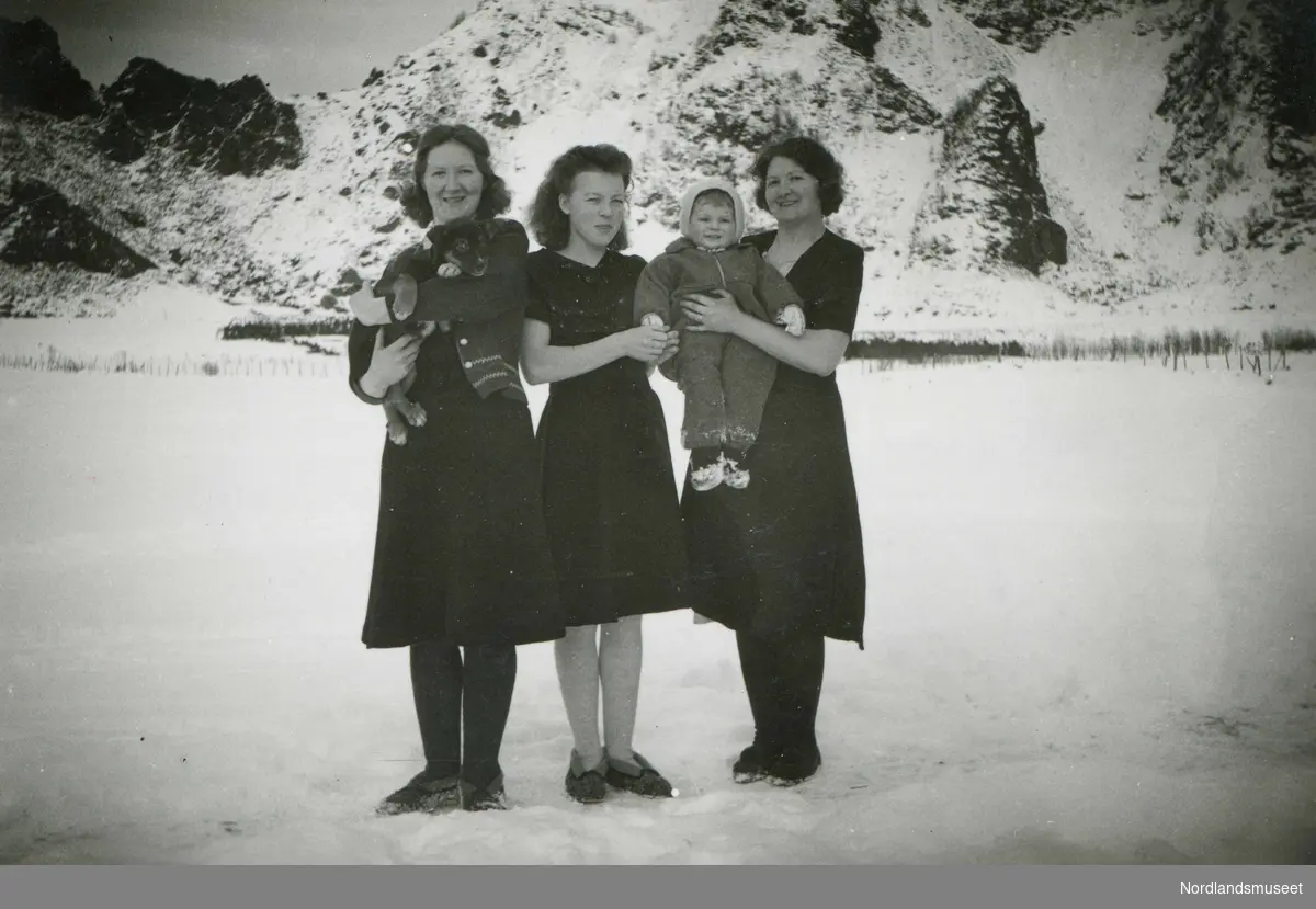 Tre kvinner, et barn og en hund fotografert på Steigberget på Engeløya i Steigen. Fra venstre Leonora (Nora) , Anna, Josefa (Siffa) og Else Marie Svendsen. Nora og Siffa var tvillinger, født i 1905. Anna (f. 1924) var deres niese og Else Marie (f. 1943) var Annas datter.