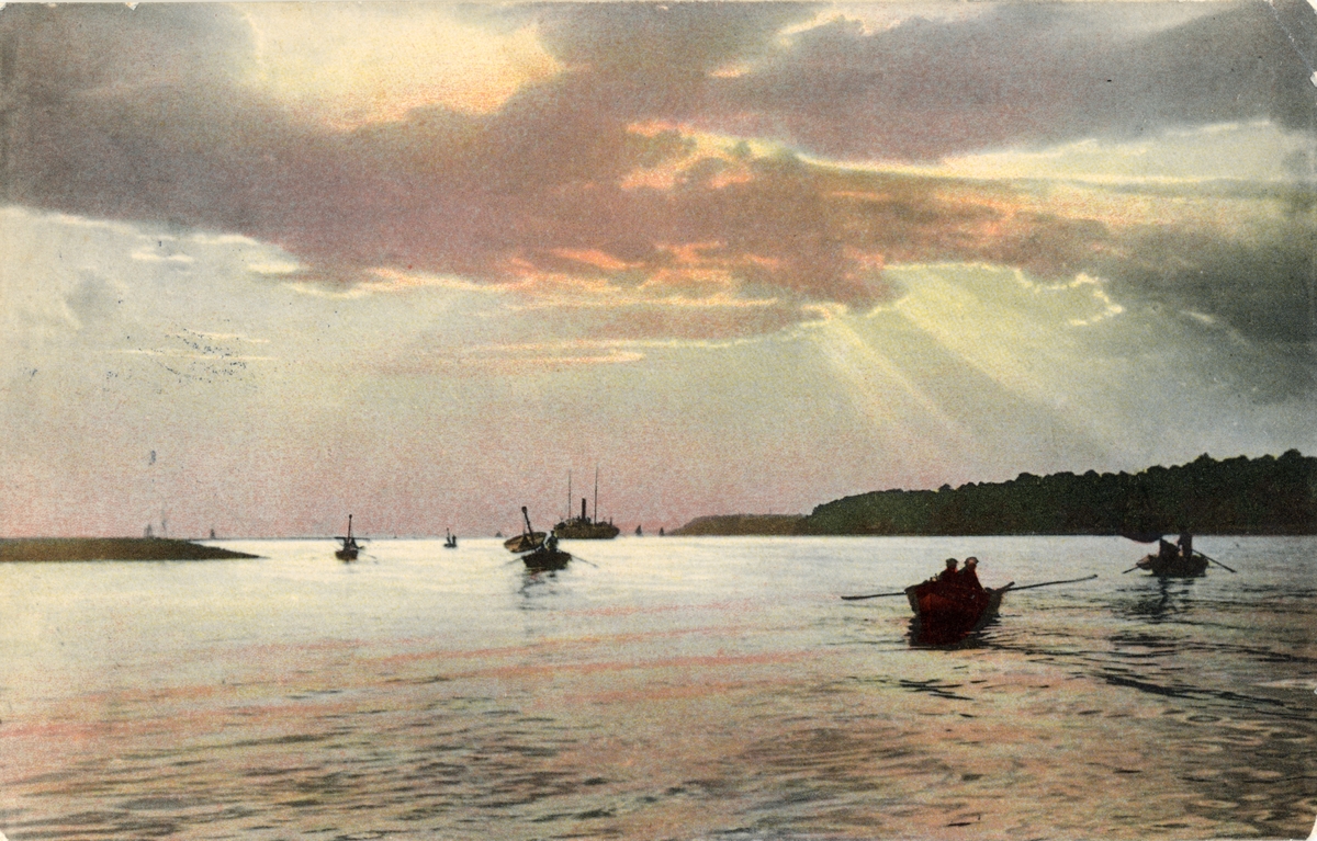 Skärgårdmotiv med solnedgång. I förgrunden roddbåtar. Vykort, färglitografi.