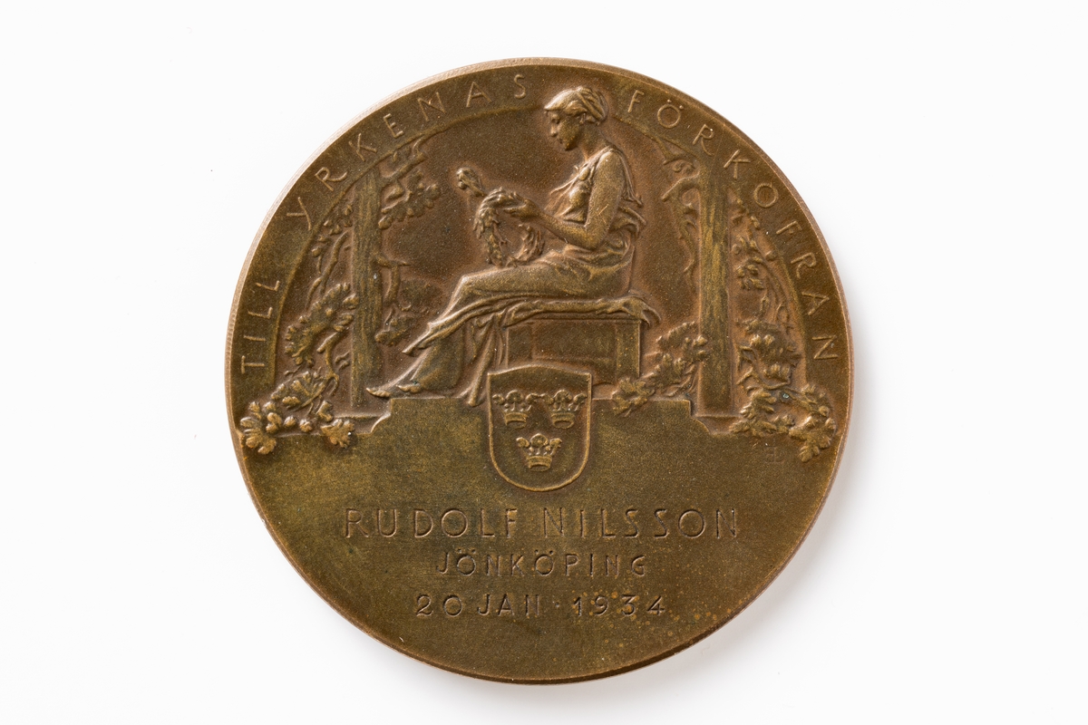 Medalj av kopparfärgad metall. På åtsidan bild av kung Gustaf V. Runt kanten text: GUSTAF V SVERIGES HANTVERKSORGANISATIONERS BESKYDDARE. På frånsidan bild av sittande kvinna med en lagerkrans, och vapensköld med tre kronor. Bilden är signerad EL. Upptill runt kanten text: TILL YRKENAS FÖRKOFRAN. På nedre halvan text: RUDOLF NILSSON JÖNKÖPING 20 JAN 1934.

Medaljen förvaras i en liten rödfärgad ask med sammet invändigt, och metallknäppe.
