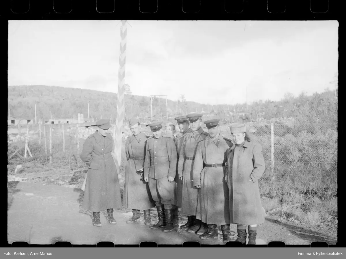 En gruppering russiske soldater poserer for et foto på grensa i Sør-Varanger ved grensebom i Storskog.  

Mann som er nr. 2 fra venstre har et kamera festet til belte 

Helt til høyre kan man se en kvinne som antagelig tilhørte det Sovjet-russiske militæret 