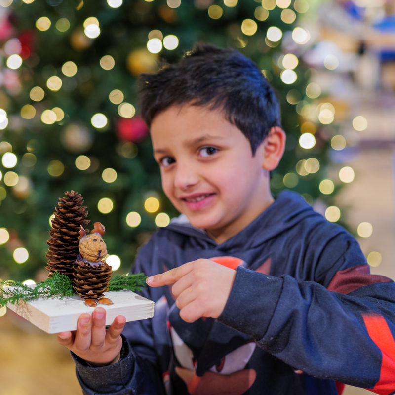En 6 år gammel gutt holder en juledekorasjon som han laget i en juleverksted