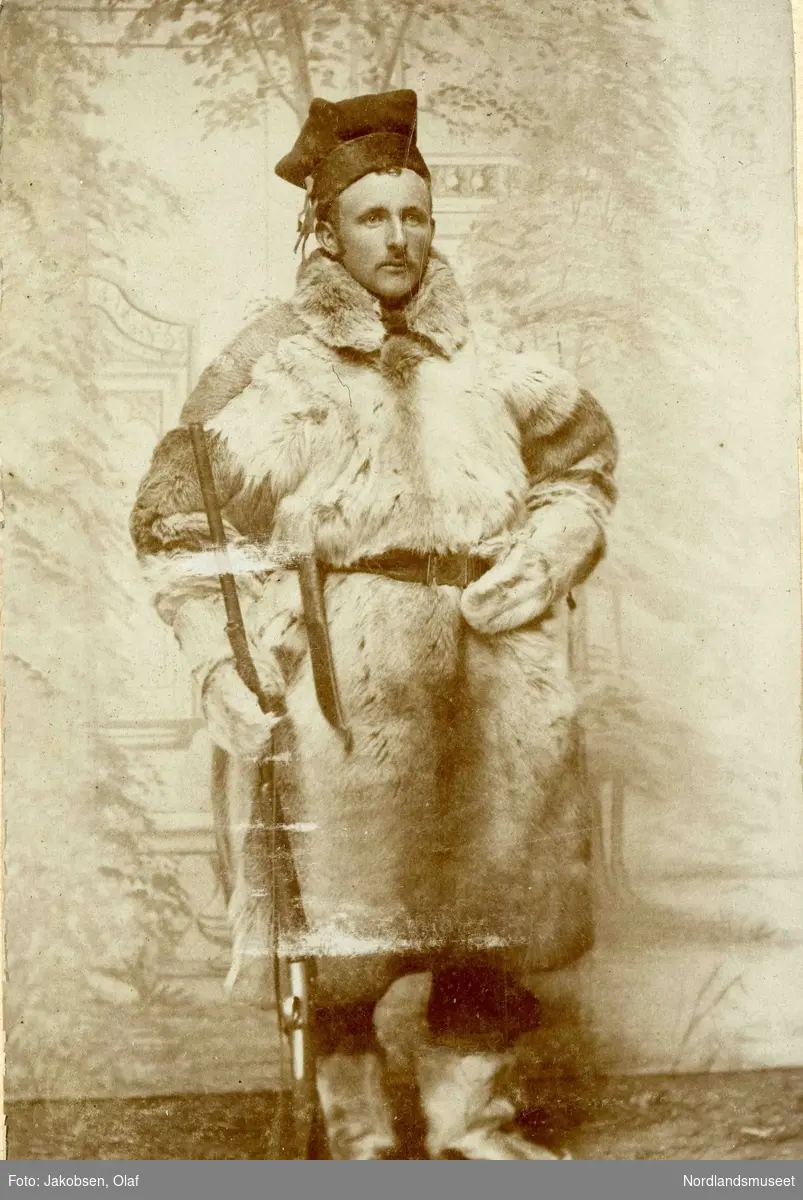 Mann kledd i pesk, skaller og samelue. Han har samekniv og gevær. Portrett av Hans Martin Korneliussen, født 1879, fra Lund i Leiranger. 