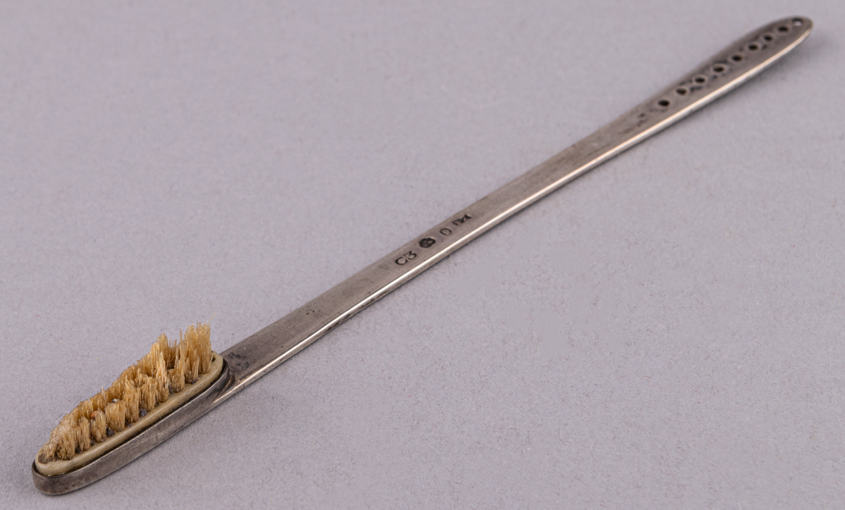 Tandborste med silverskaft, stämplat: C3, kattfot, PZ. Platt med 9 små runda hål i rad i handtagsänden. Själva borstens hållare 2,4 cm lång. Tillverkad av Pehr Zethelius, Stockholm år 1809.