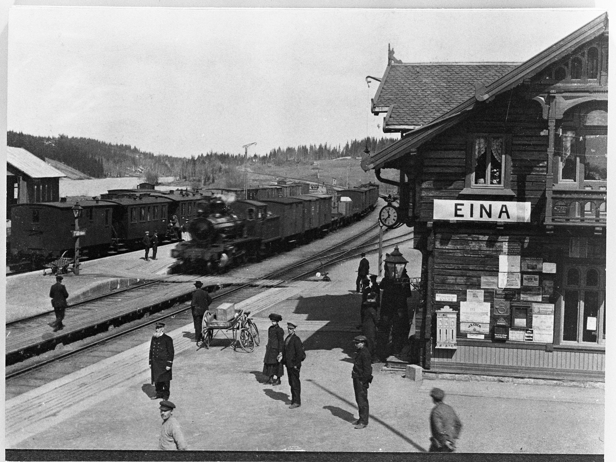 Postkort med motiv fra Eina stasjon 1911. Folk på perrongen, og tog på skinnene.