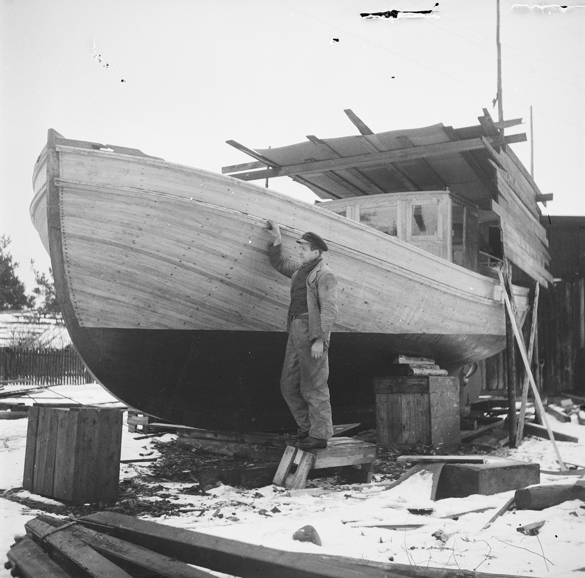En man står vid en uppställd fiskebåt, Hällnäs, Uppland