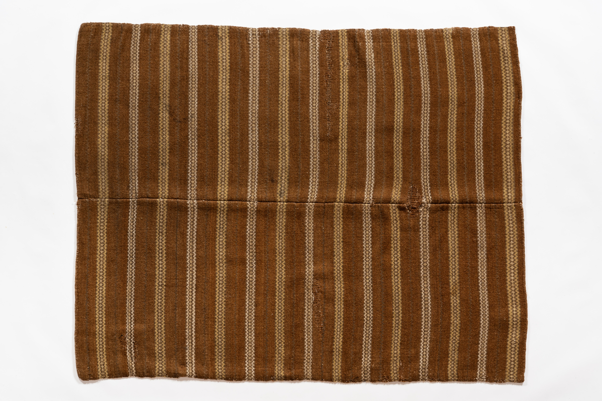 Täcke, bragdatäcke av ull i inslag och lin i varpen. Täcket är vävt i två delar och skarvat på mitten. Mönstrat i rosengångsränder i gult, brunt, rödbrunt och vitt.