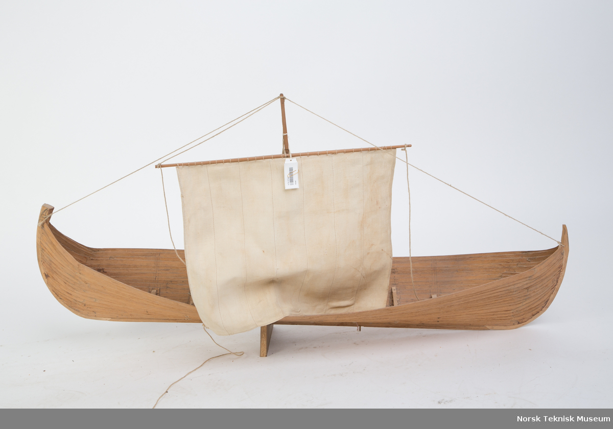 Modell av vikingskip med mast og seil.