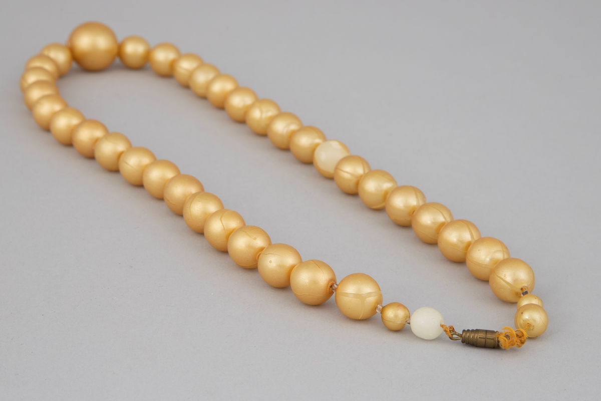 Halskjede bestående av 39 gule perler med små glassperler imellom. Perlene er ordnet med 19 på hver side av en større perle. Av de 19 er 17 omtrent like store, mens de to nærmest låsen er mindre, hvorav den største er nærmest låsen. Enkel gullfarget skrulås.