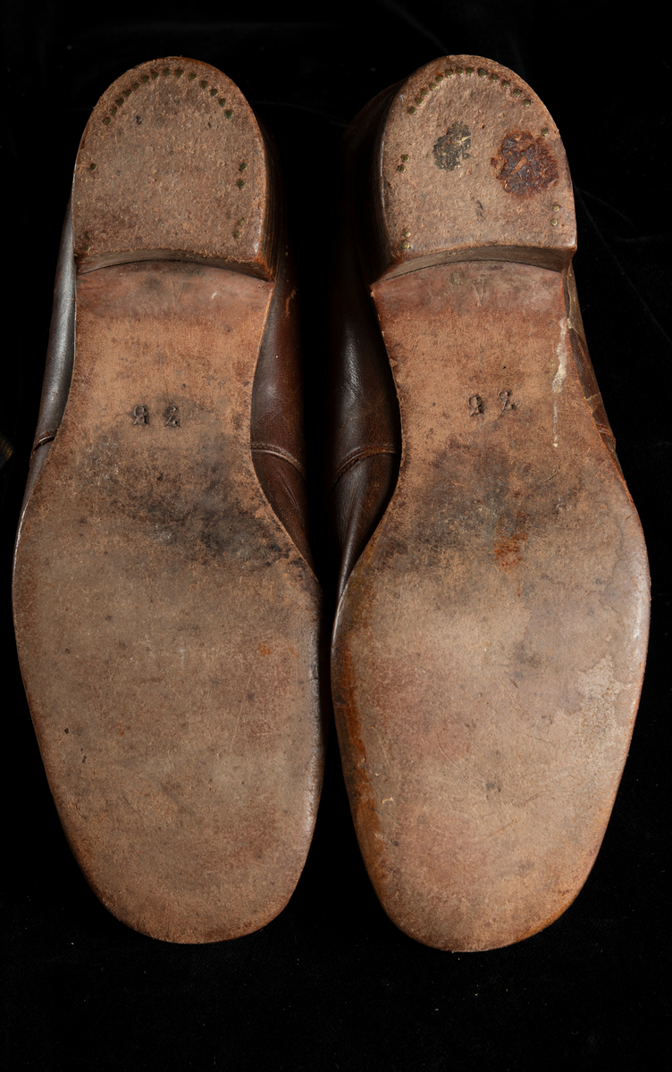 Ett par skor av brunt skinn. Flickmodell i storlek 35. Klackhöjd 25 mm. Dubbla slejfar som knäpps med små bruna plastknappar.