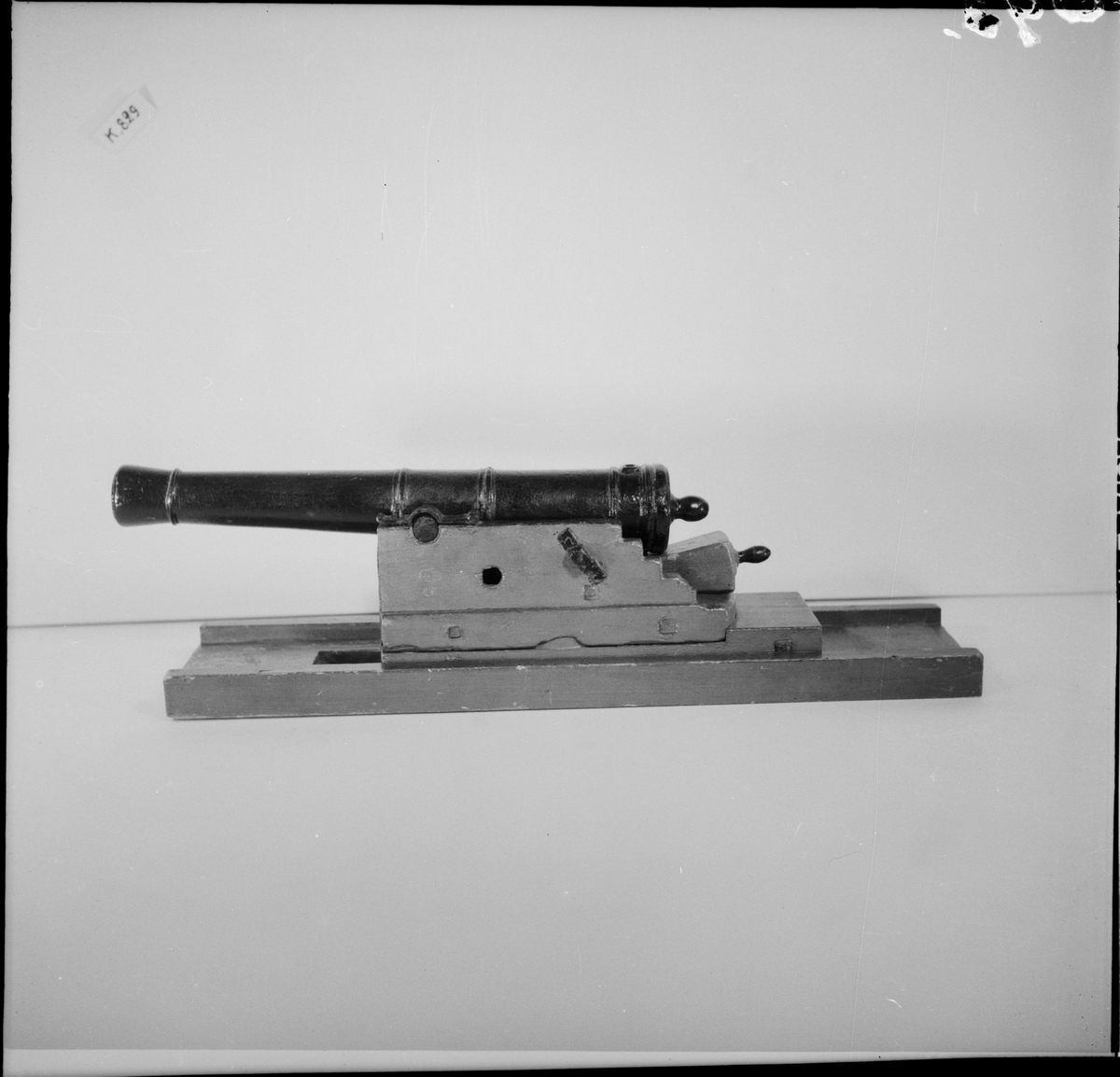 Kanonmodell: galérlåda med släde, beslagen, samt kanon. Lavetten av trä, rödmålad. Kanonen av järn, svartmålad. Tillbehör: 1 st ställhult. Lavetten L = 440 mm B = 110 mm H = 130 mm.