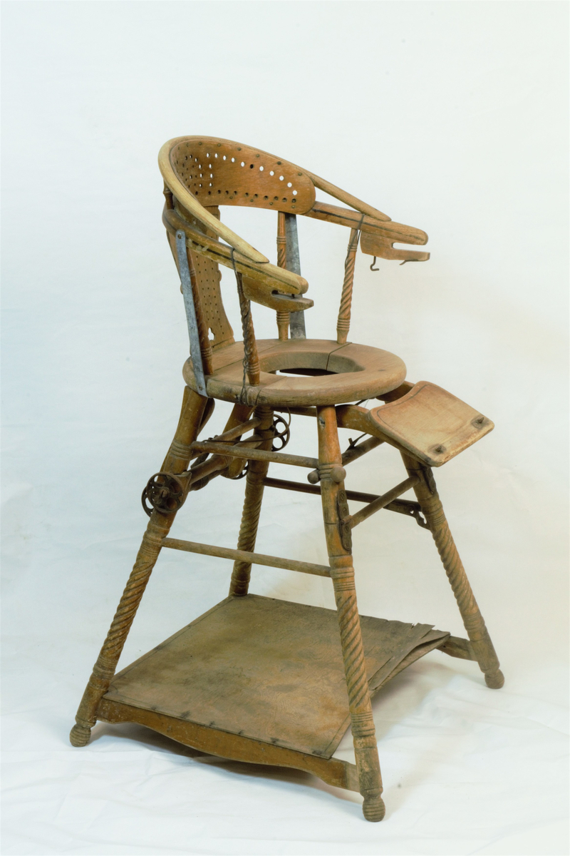 Barnestol med to funksjoner i en, siden den kan brettes ned til en liten lekestol med bord. Påfestede hjul som kan brukes til å trille den rundt når den er nedbrettet. Armlenene har på et tidspunkt blitt forsterket med metallstenger og metaltråd.