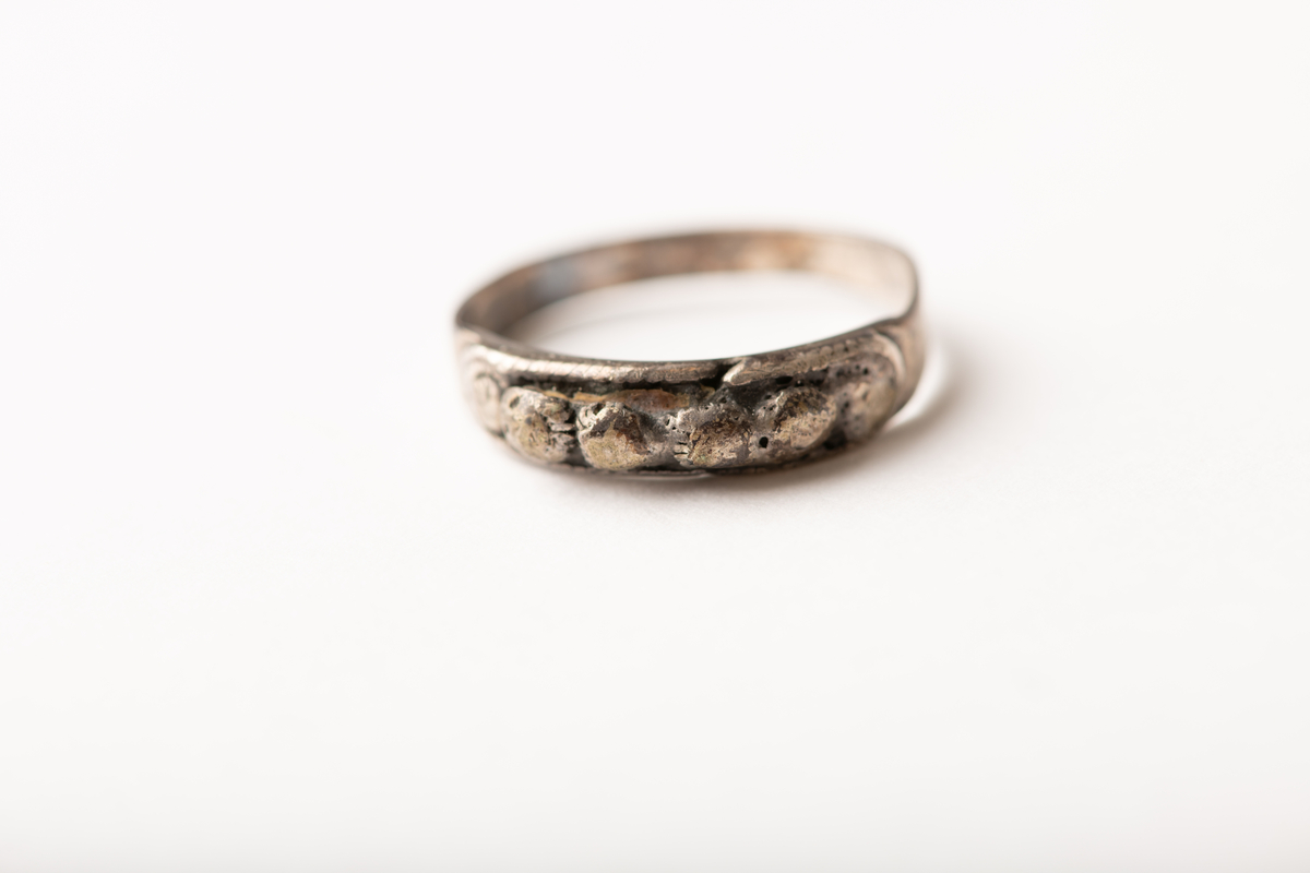 Tynn båndformet ring med påloddet plate med fire sølvperler, flankert av to flatere.