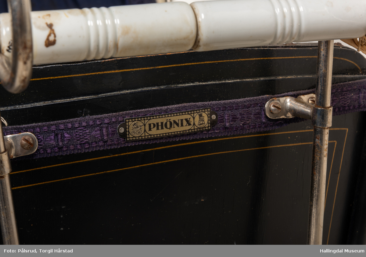 Sort barnevogn fra 1920-tallet. Gullborder på sidene og mørk blå forheng forran "hetta". Av merke Phönix.
