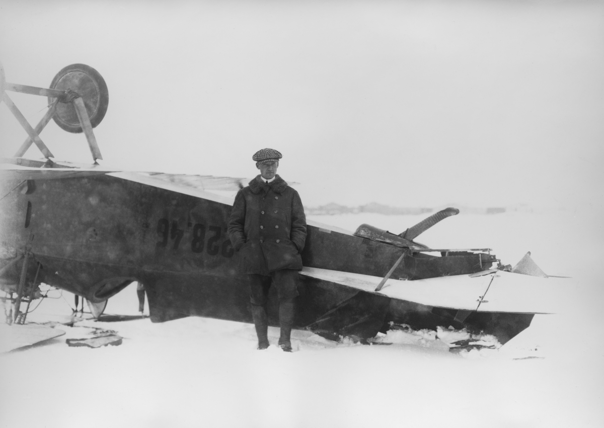 Edmund Sparmann står framför havererat militärt flygplan Phönix D.I märkt 228.46 tillhörande Österrike-Ungern, Flygplanet har hamnat på rygg. Vintertid. Vy från sidan.