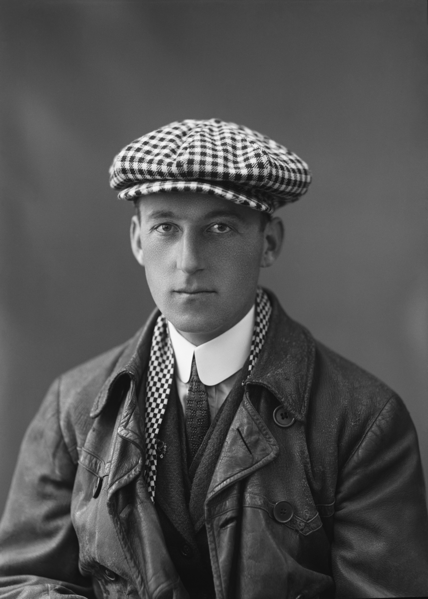 Porträttfoto av Edmund Sparmann i kostym, halsduk, keps och flygarjacka i studiomiljö, omkring 1914-1918.