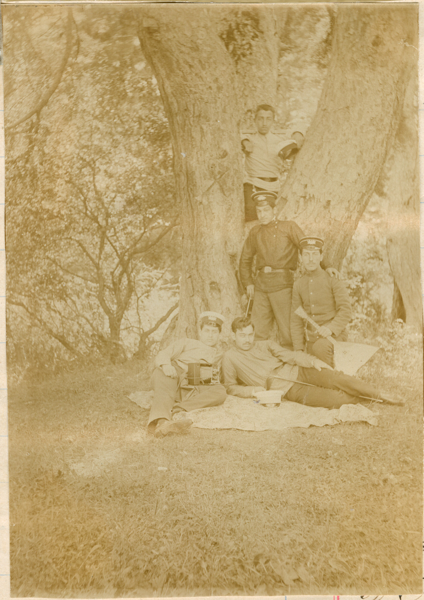Motivet viser fem uniformerte yngre menn i en park. To av mennene har tatt av seg luene sine. Den ene mannen holder en balalaika. To ligger på et teppe, to står oppreist og en poserer i et tre.