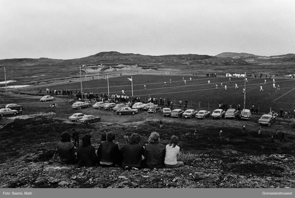 Fotballkamp på Mosedalen stadion, Bølgen sin hjemmebane på Bugøynes.. Publikum står langs banen, sitter i biler og oppe på fjellet.