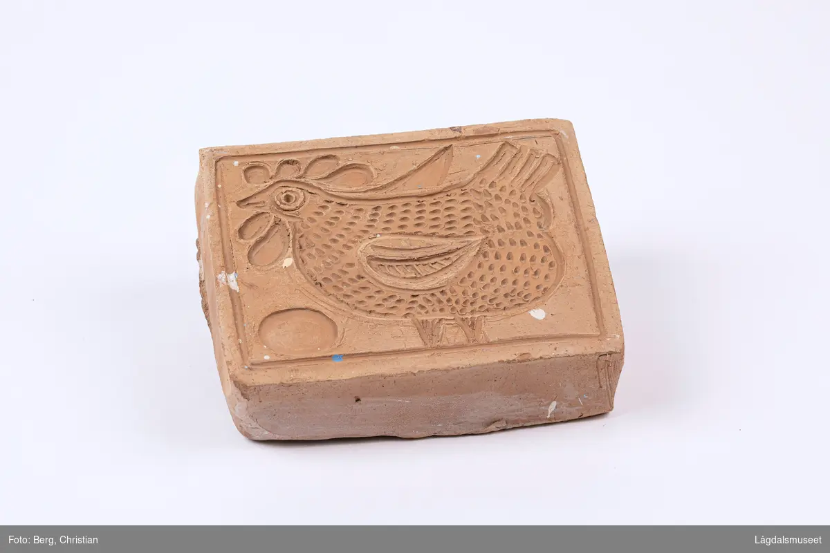 Trykkblokk i keramikk for enkelt å påføre dekorelement på fat og lignende. Motivet er ei høne og et egg.