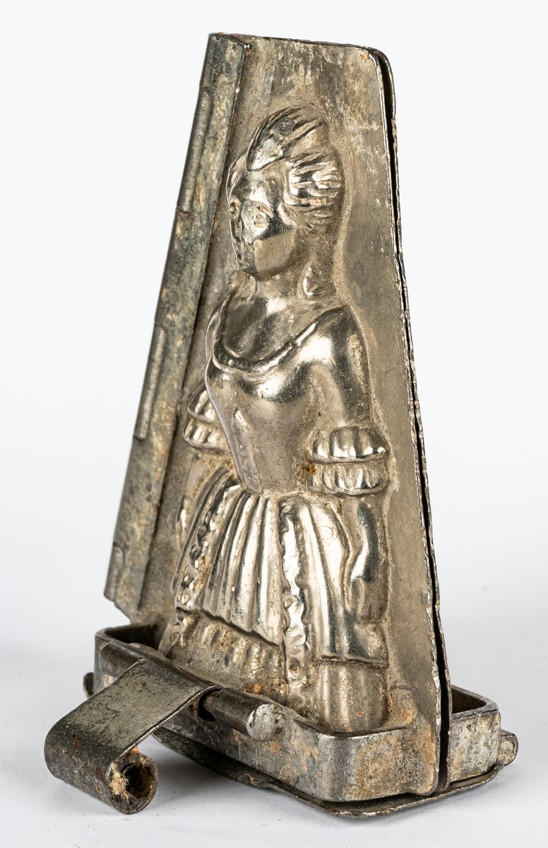 Gjutform i nickel, för choklad, föreställande en kvinna i 1700-talsklänning. Gångjärn i sidan på formen. Tillverkad av Henri Le Cerf i Köln, Tyskland.